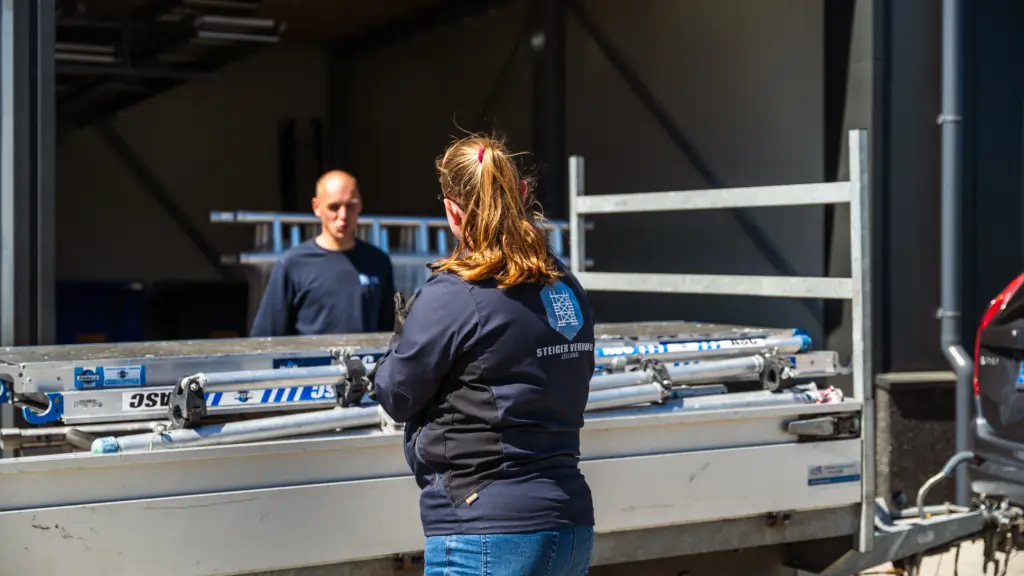 Het team in overleg langs een steigeraanhanger